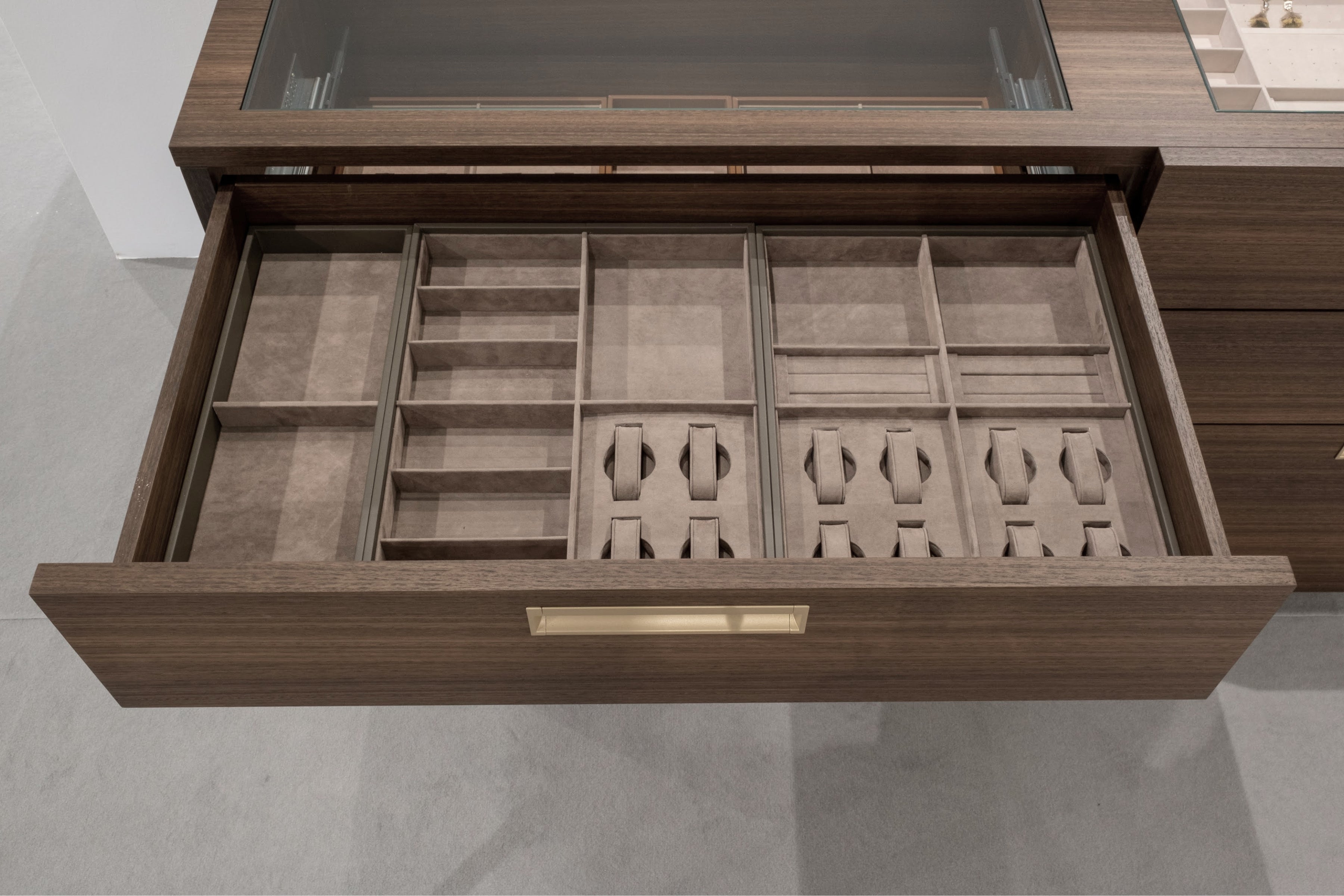 An open wooden organizer drawer with multiple compartments and tie-down loops, shown from above against a modern gray background.